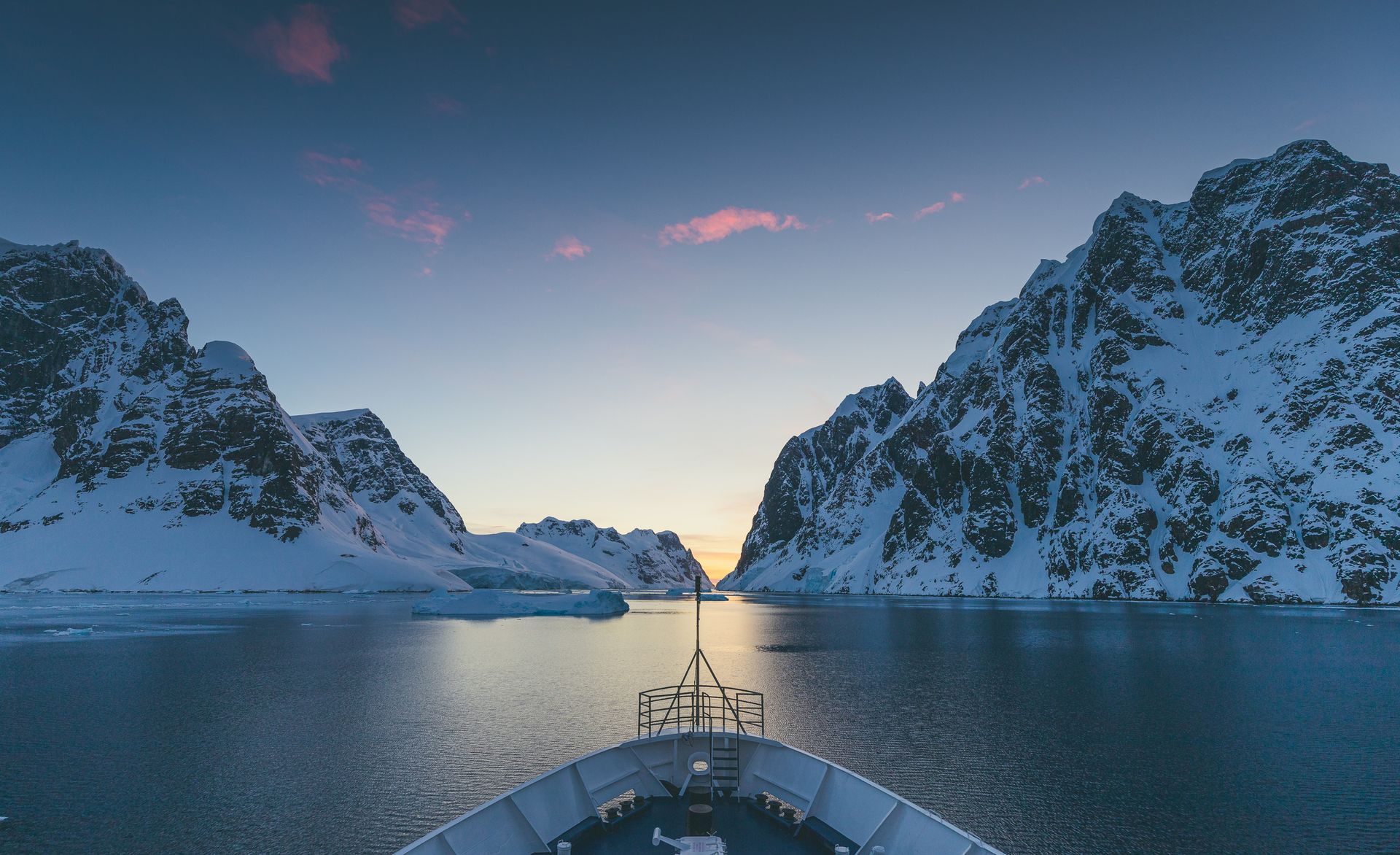 Ship sailing through snowy mountain passage at dusk.