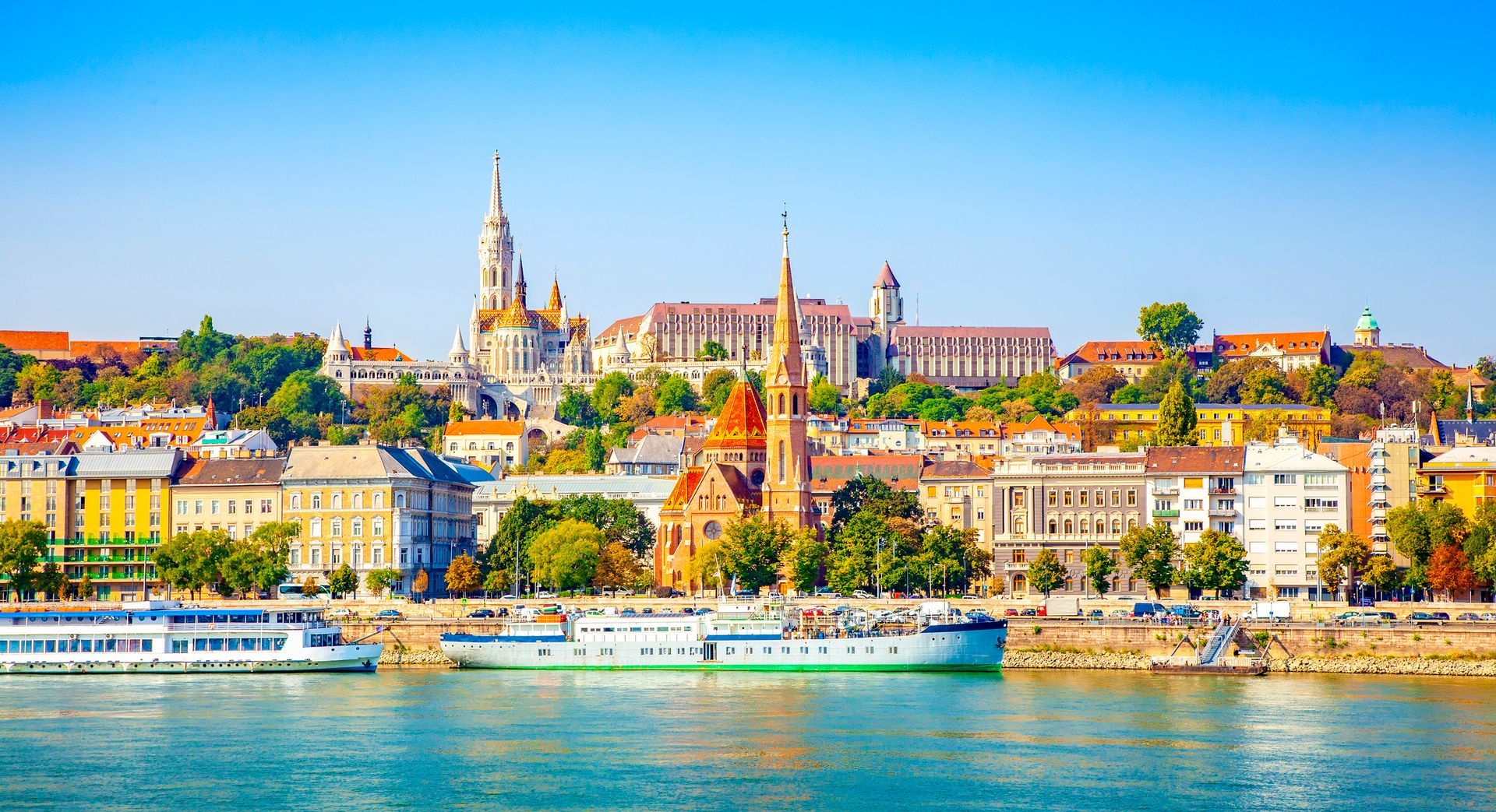 Budapest cityscape with boats on the Danube River, showcasing buildings and blue sky.