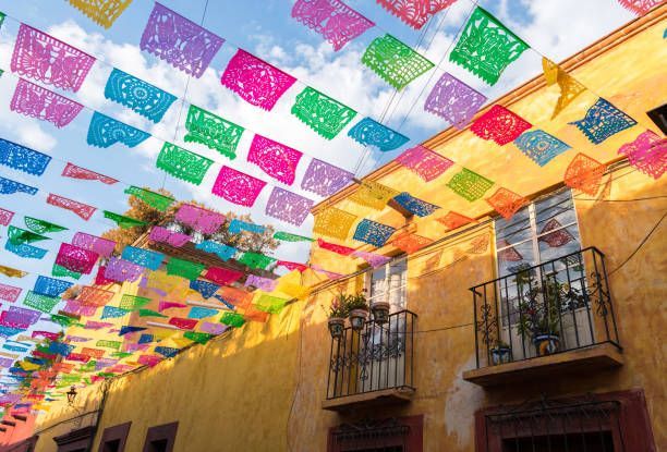 Colorful papel picado banners strung above a sunlit building with balconies.