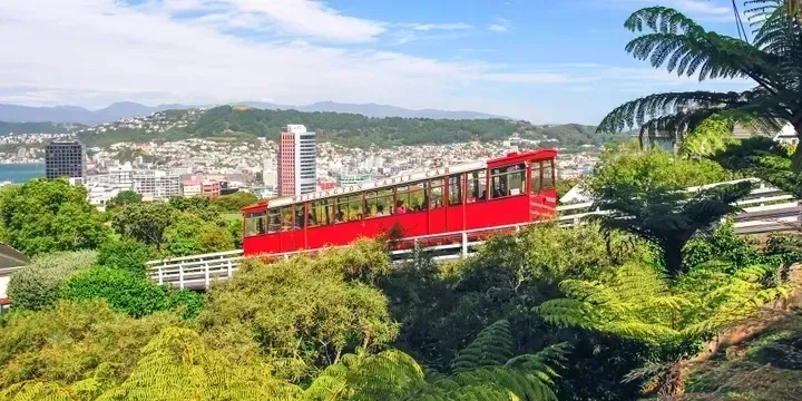 A modern cruise ship cabin with a bed, TV, balcony, and seating area.