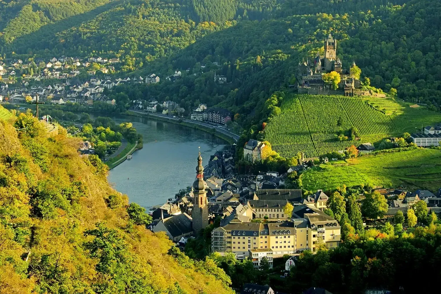 Scenic view of a town nestled between hills, with a river running through. A castle sits atop a hill.