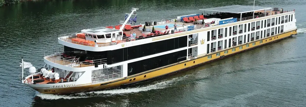 A large, gold and white river cruise ship sailing on a dark blue river.