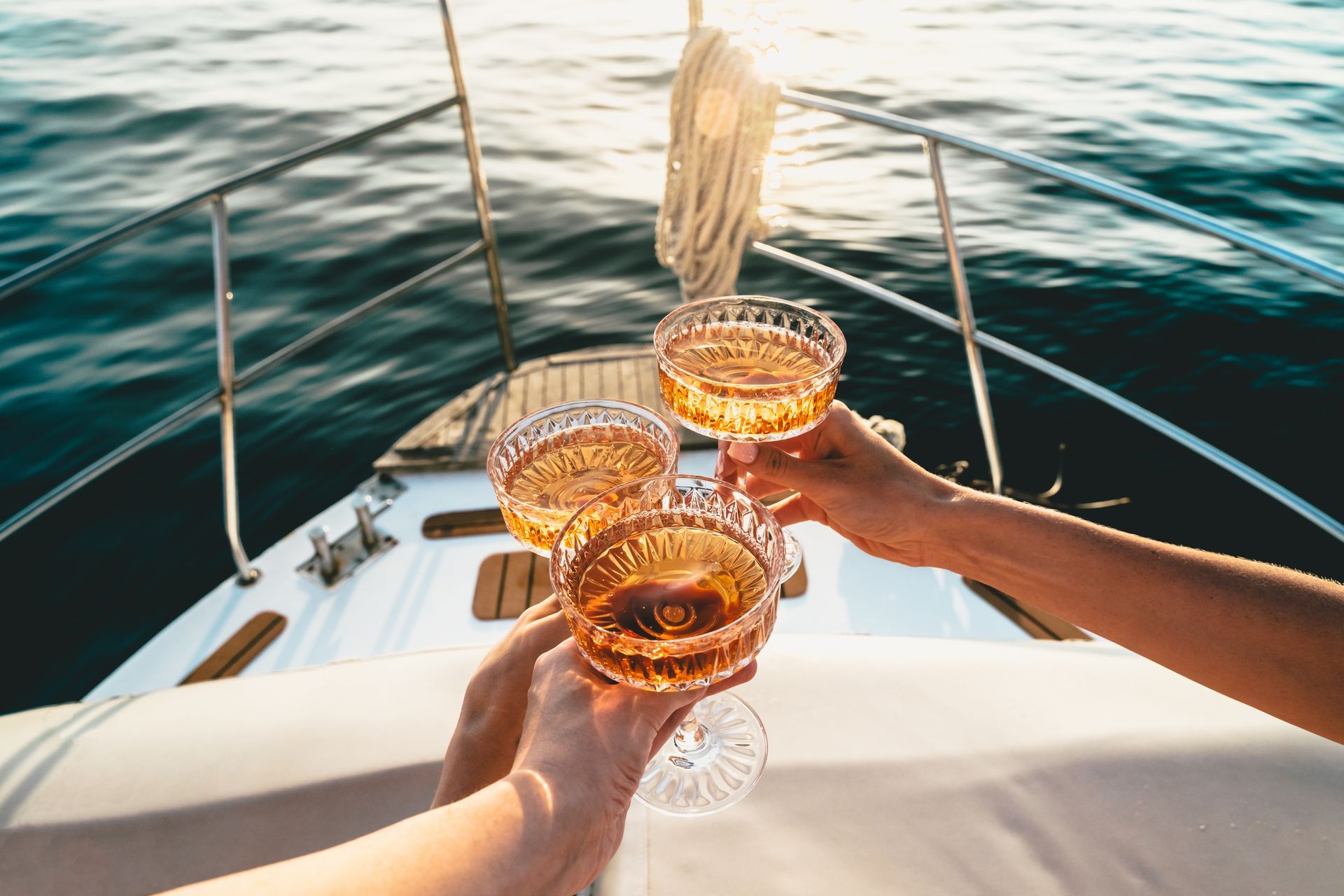 Three people toasting champagne glasses on a boat, ocean in the background.
