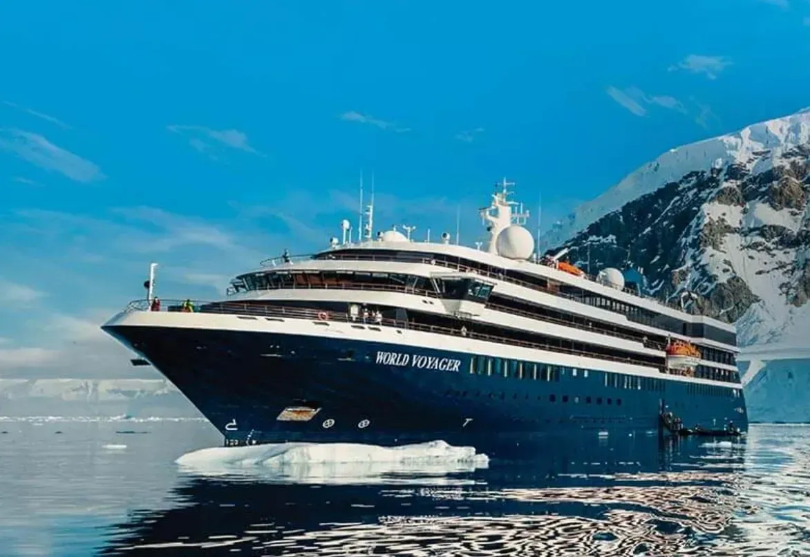A cruise ship sailing near icy mountains and glaciers, against a bright blue sky.