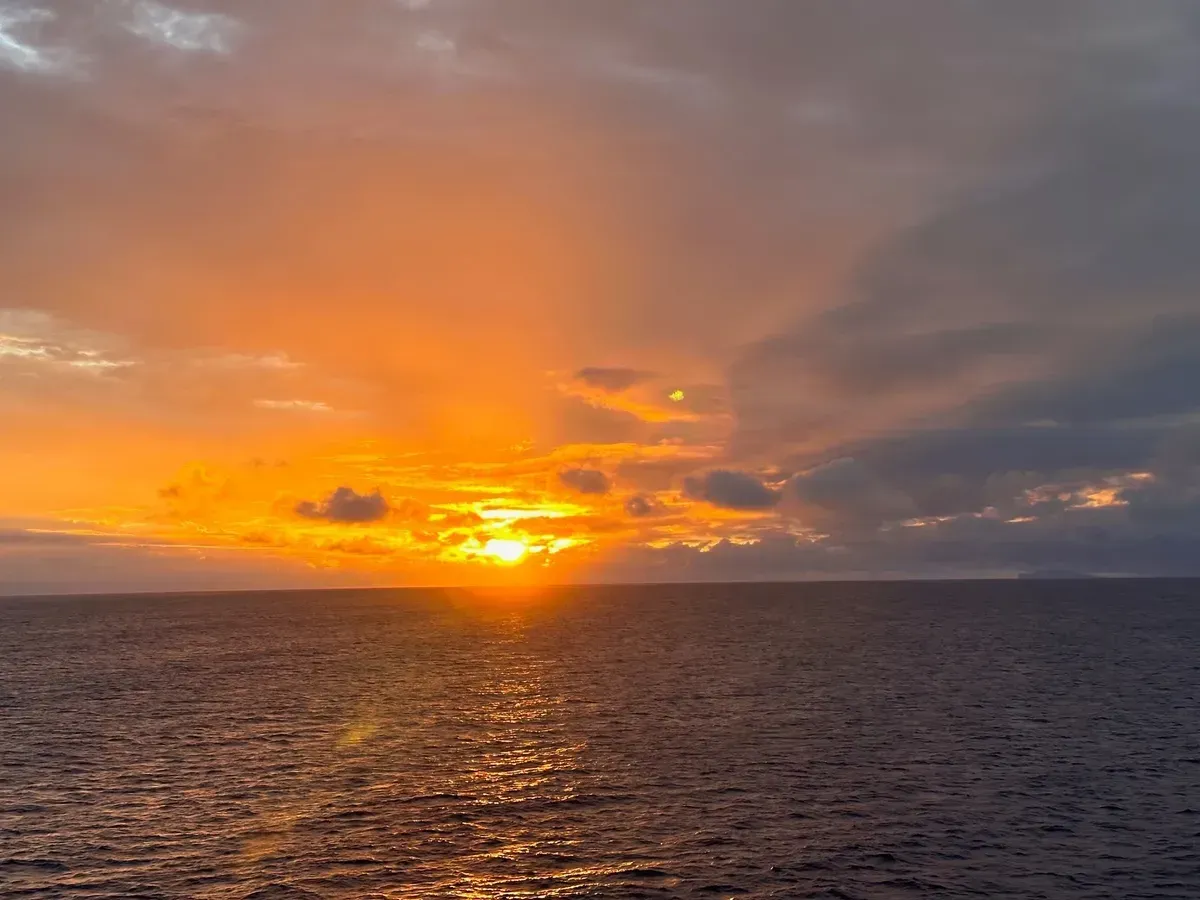 Sunset over the ocean, with orange and yellow sky reflecting on the water.