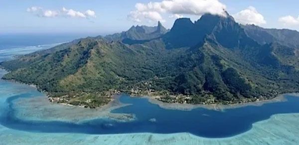Island landscape with lush green mountains, blue ocean, and clear skies.
