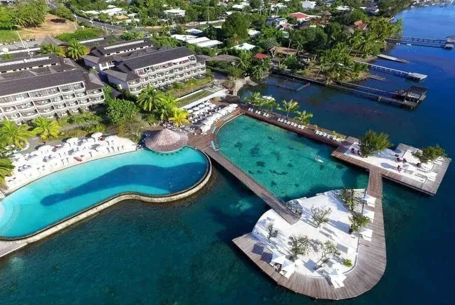 Aerial view of a resort with pools, white lounge areas, and waterfront docks with the clear blue sea.