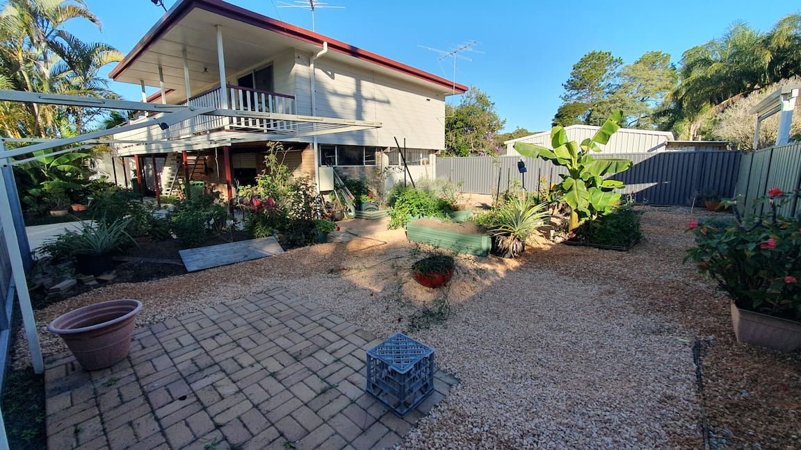 A large white house with a red roof is surrounded by a lush green garden.