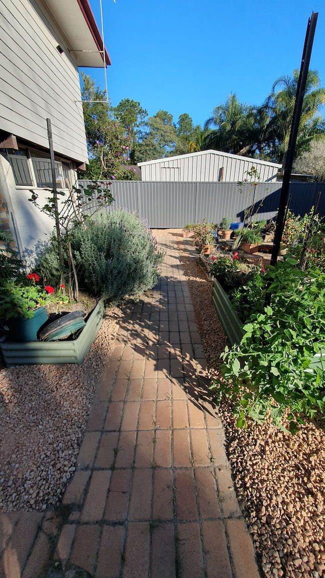 A brick walkway leading to a house in a garden.