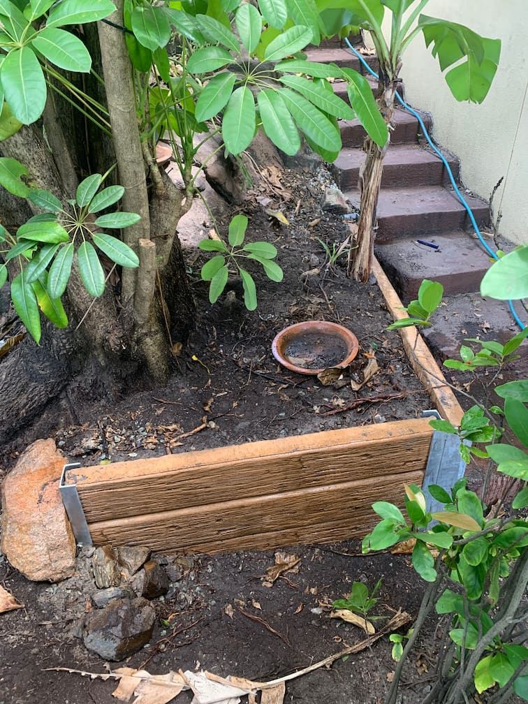 A wooden planter is sitting in the dirt next to a tree.