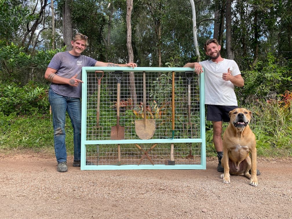 Two men and a dog are standing next to a fence.