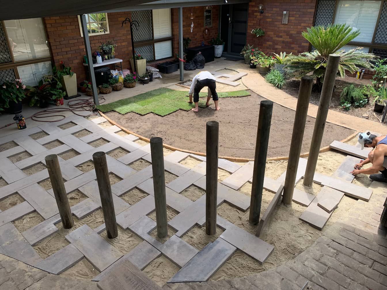 A man is laying tiles on a patio in front of a house.
