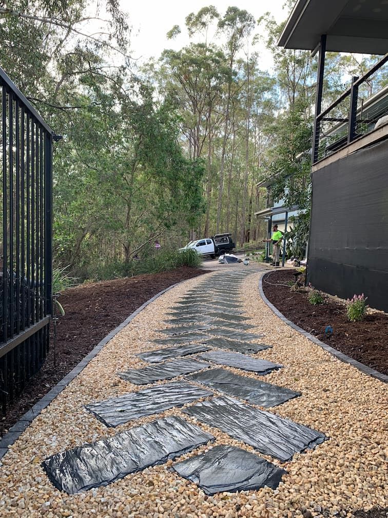 A stone walkway leading to a house surrounded by gravel and trees.