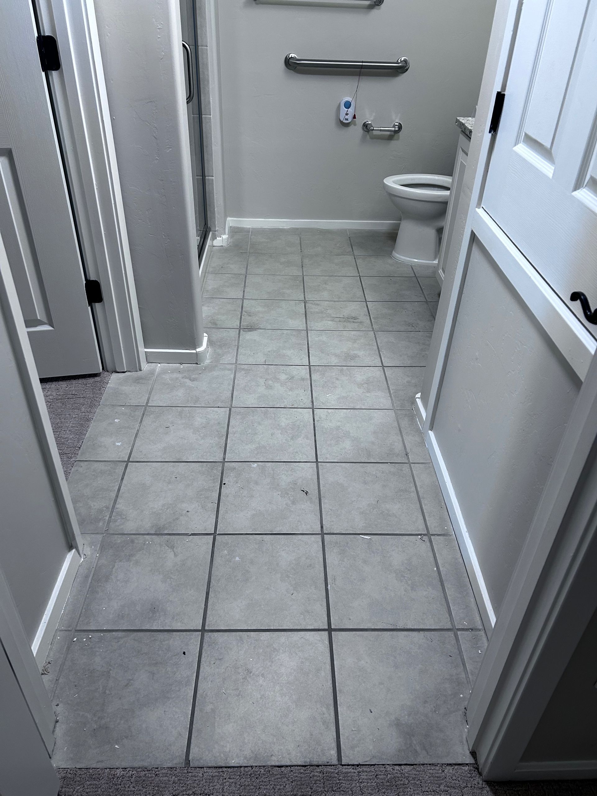 Narrow tiled bathroom hallway with open doors, a sink, and a toilet ahead