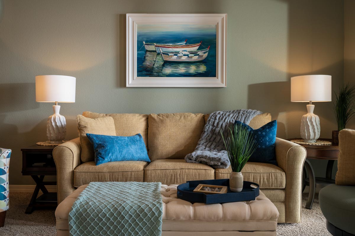 Interior design of a cozy living room set in a vacation rental with a painting of boats above the couch and blue accessories that  match the color scheme
