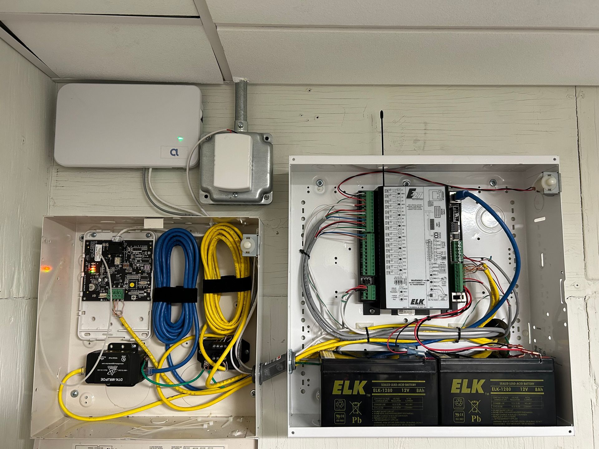 Security system components mounted on a wall: panels, wiring, batteries, and a wireless device.