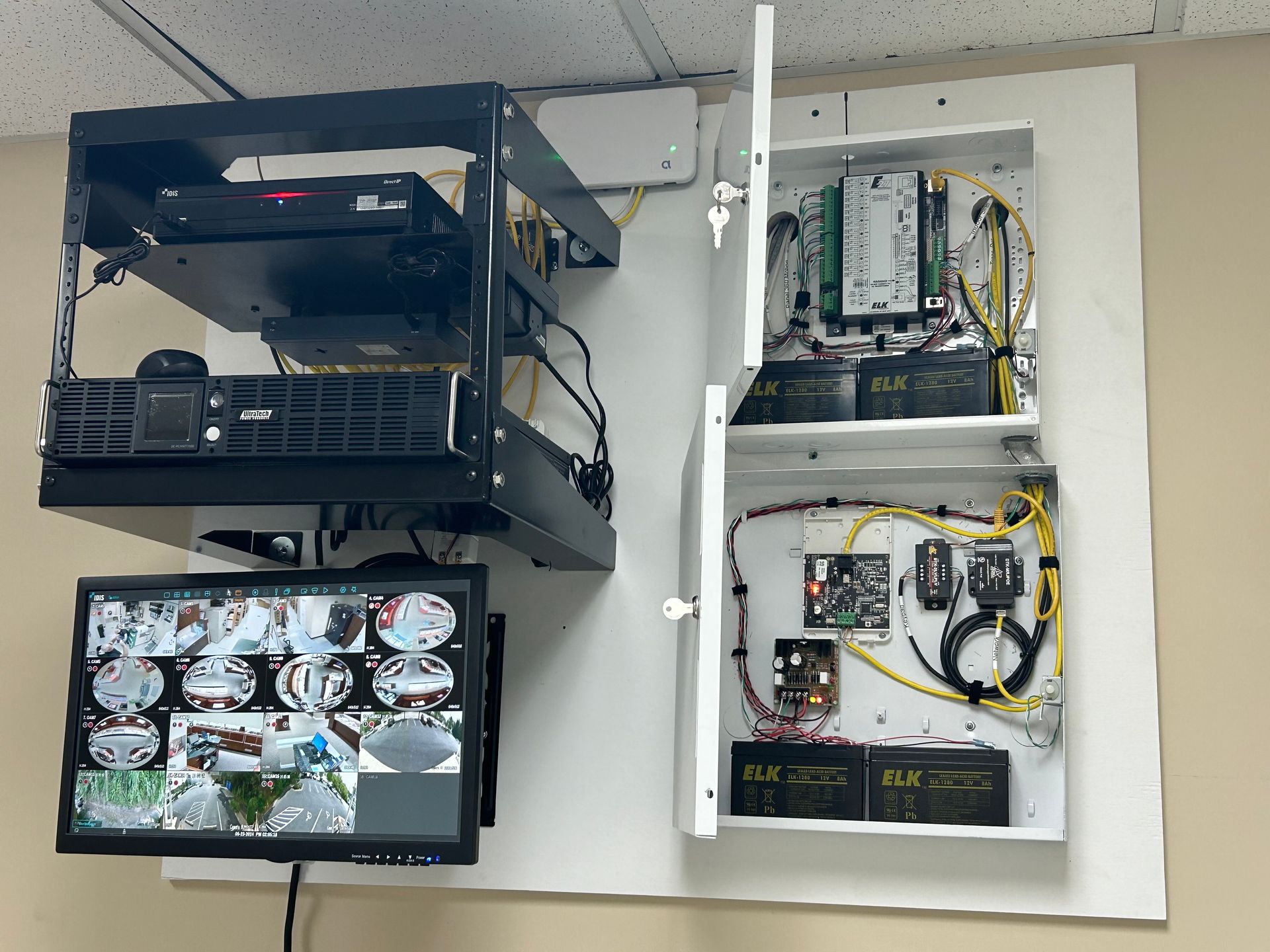 Ceiling-mounted security system with black rack holding devices, monitor, and open white cabinet with electronics.