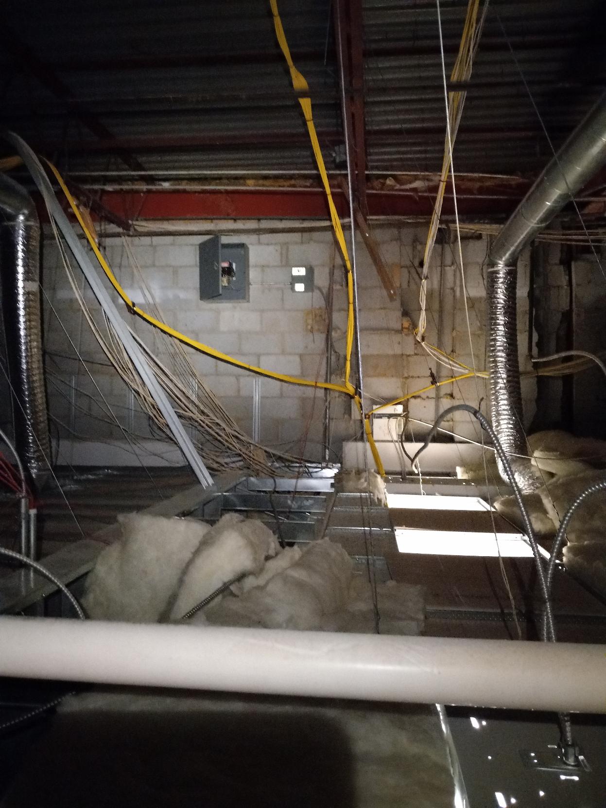 Basement ceiling with exposed wiring, ductwork, and insulation. Light illuminates through a floor opening.