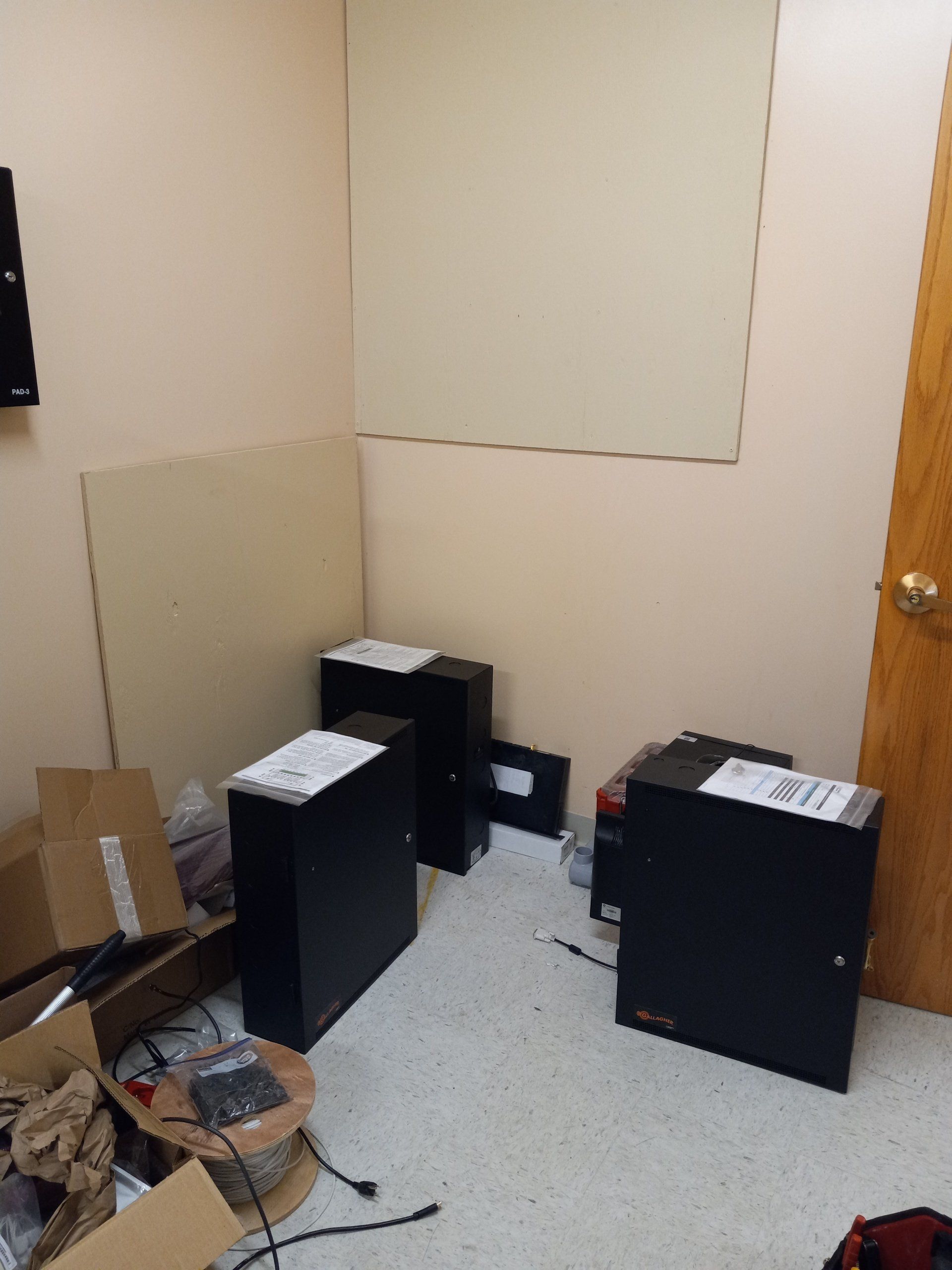 A cluttered room with four black server cabinets, cardboard boxes, and wires on the floor. 