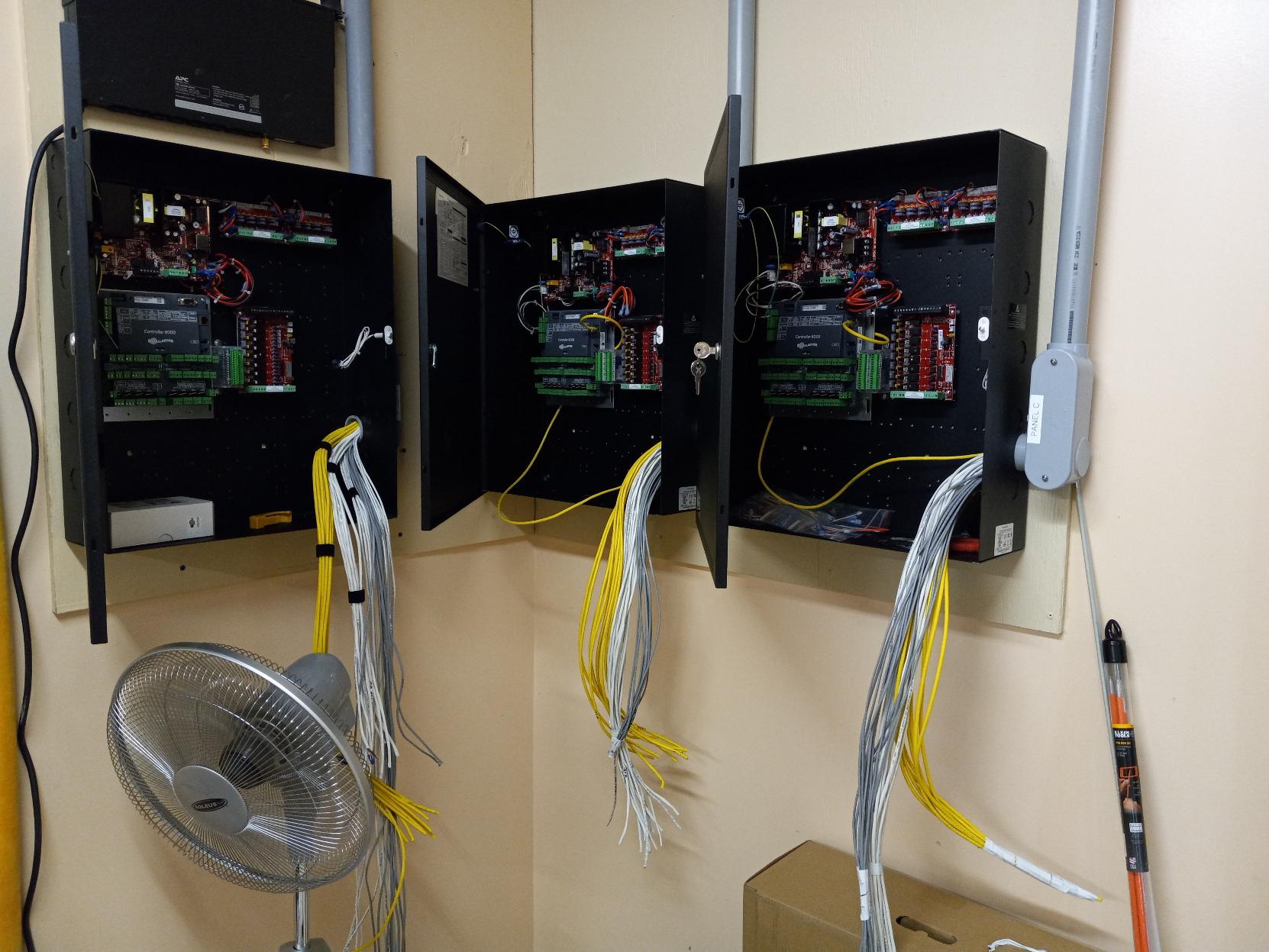 Three black electrical boxes mounted on a wall with open doors, revealing circuit boards and wiring.