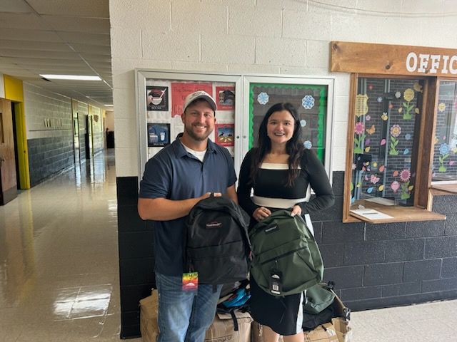 Mr. Ryan and lady holding donated backpacks