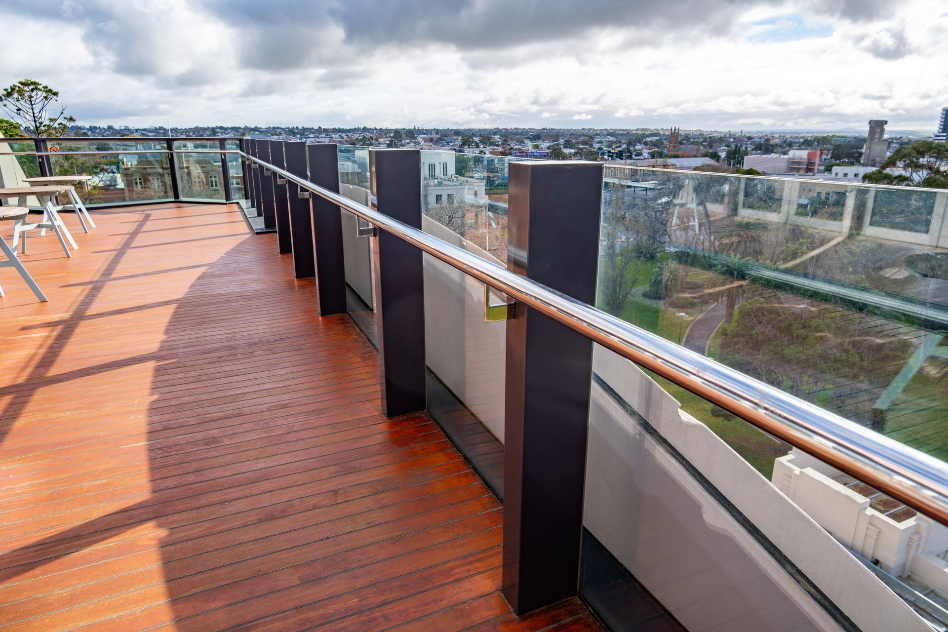 Contemporary rooftop balcony featuring timber flooring, glass balustrades, and expansive city views.