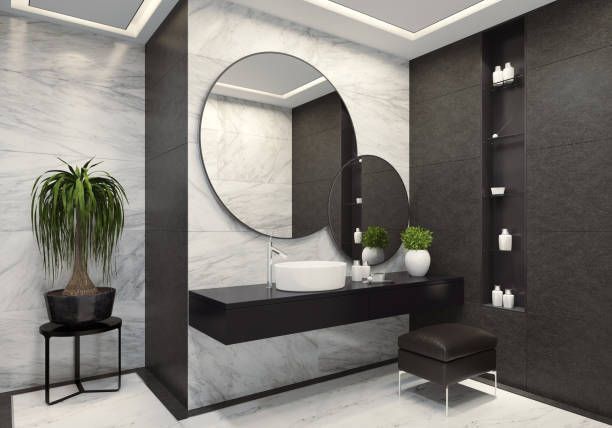 Modern bathroom with a round mirror, white sink, black vanity, and potted plants on a marble wall.