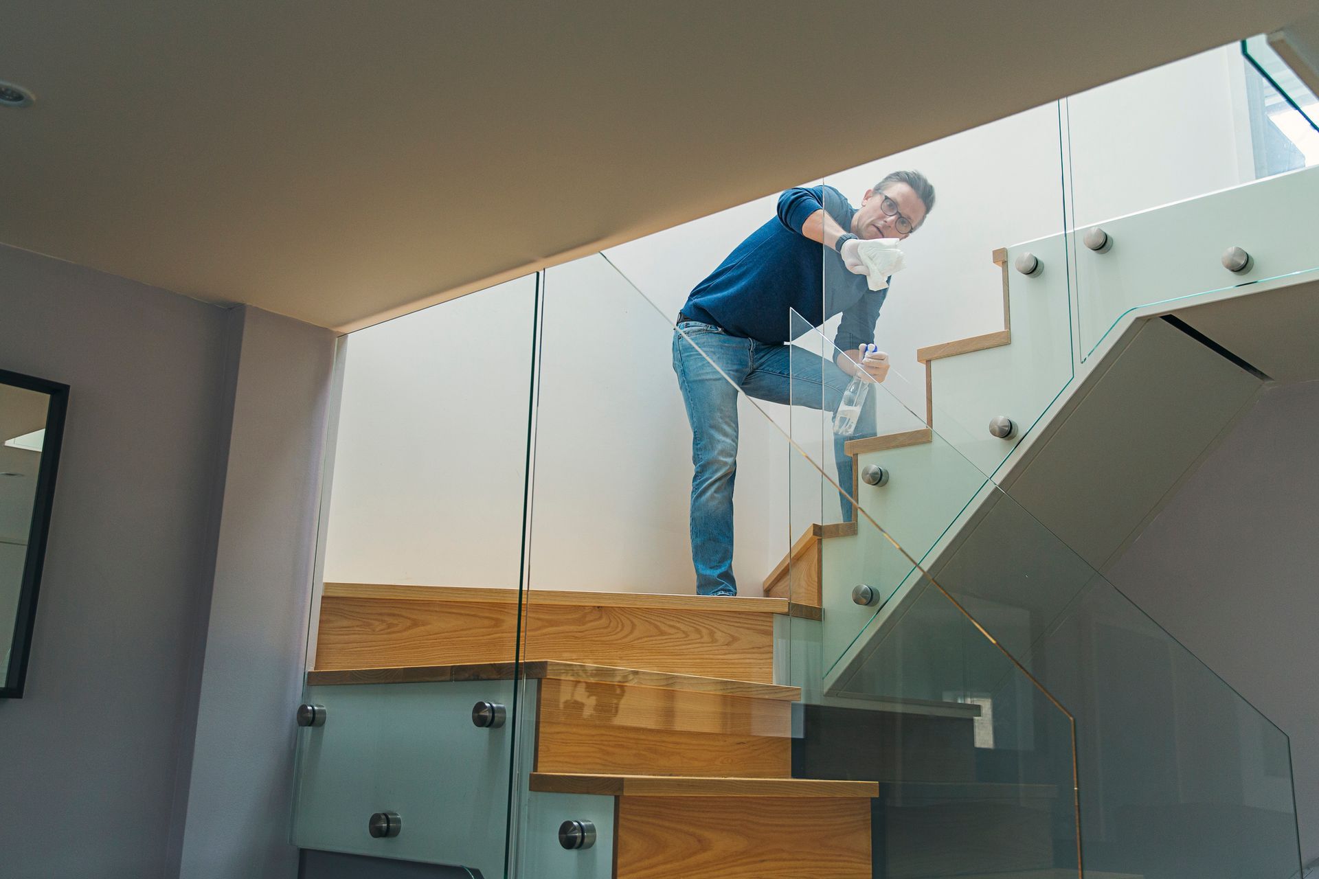 Person cleaning a glass balustrade on a wooden staircase with metal brackets. Person cleaning a glass balustrade on a wooden staircase with metal brackets.