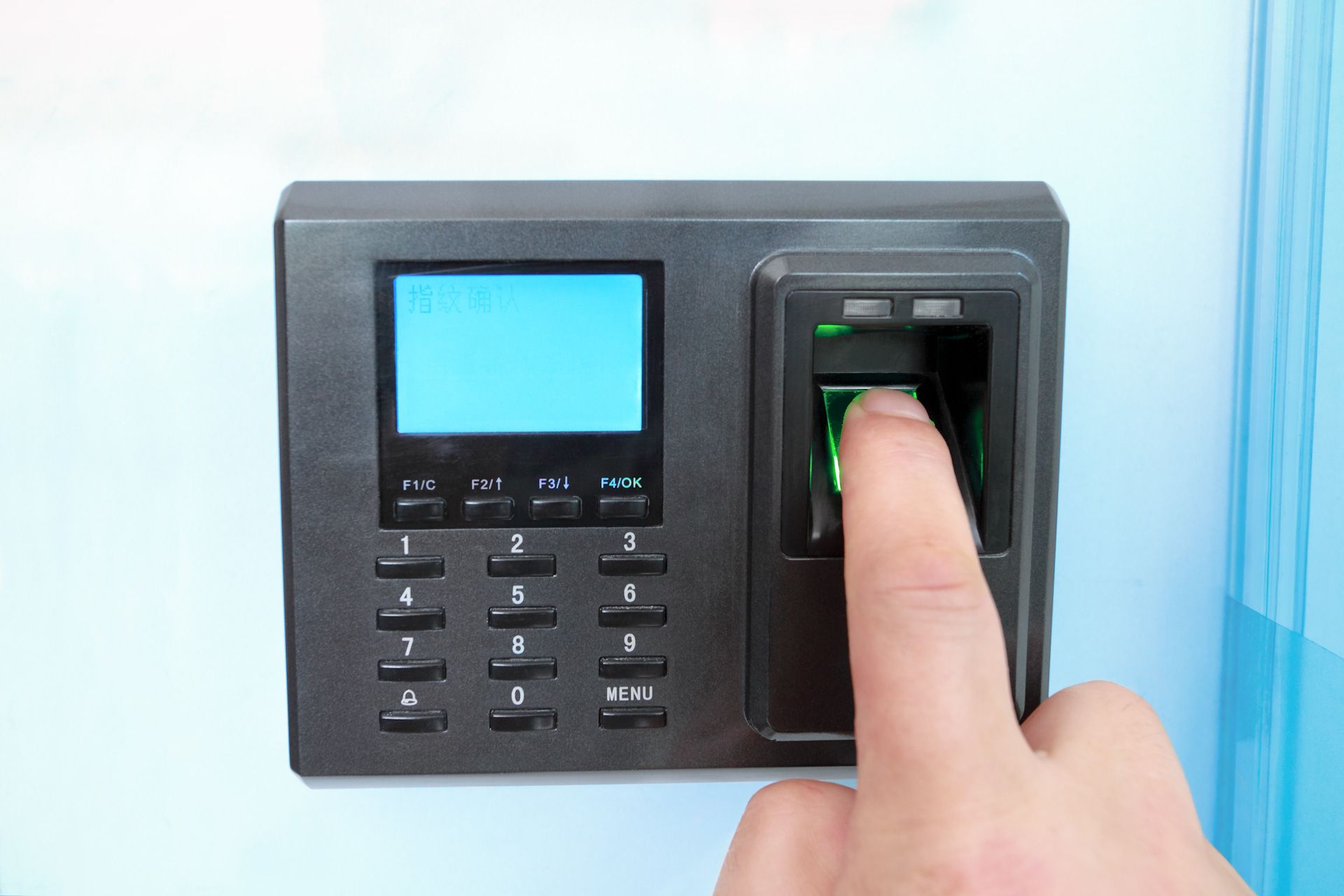 A person is using a fingerprint scanner on a wall.