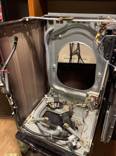 Washing machine interior with front panel open, showing components, hoses, and wiring.