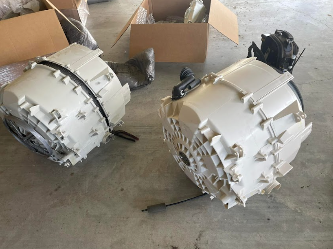 Two disassembled washing machine tubs on a gray floor, boxes in background.