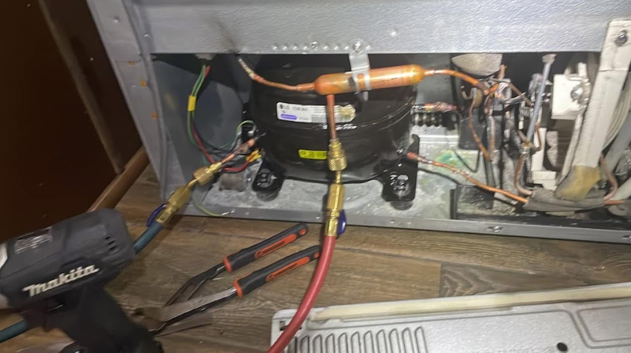Refrigerator compressor repair with hoses connected, tools nearby.