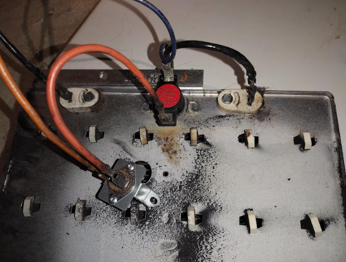 Close-up of a dryer heating element, featuring wires and a thermal fuse with signs of soot and damage.