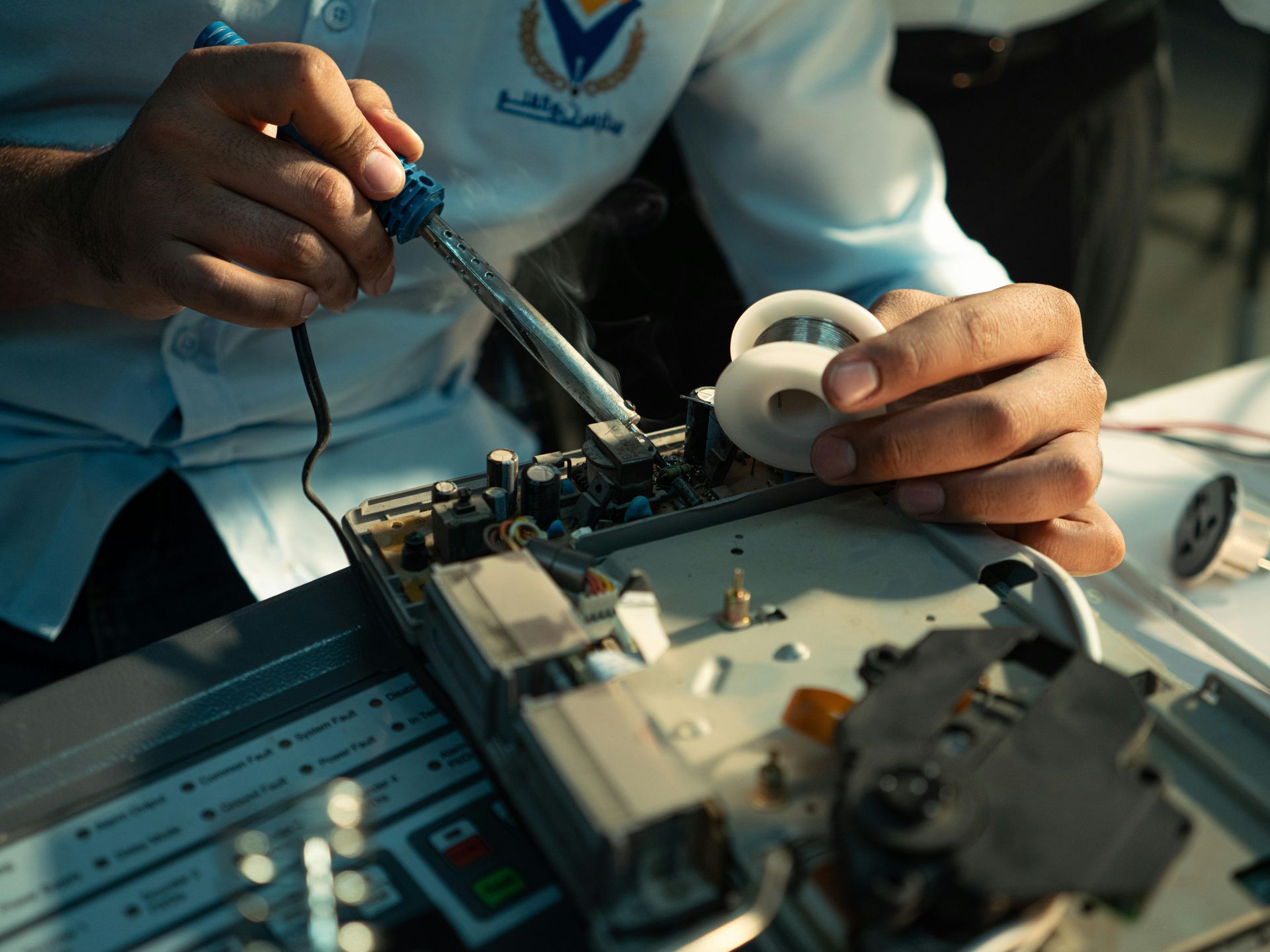 Person soldering a circuit board, holding a soldering iron and a white plastic piece.