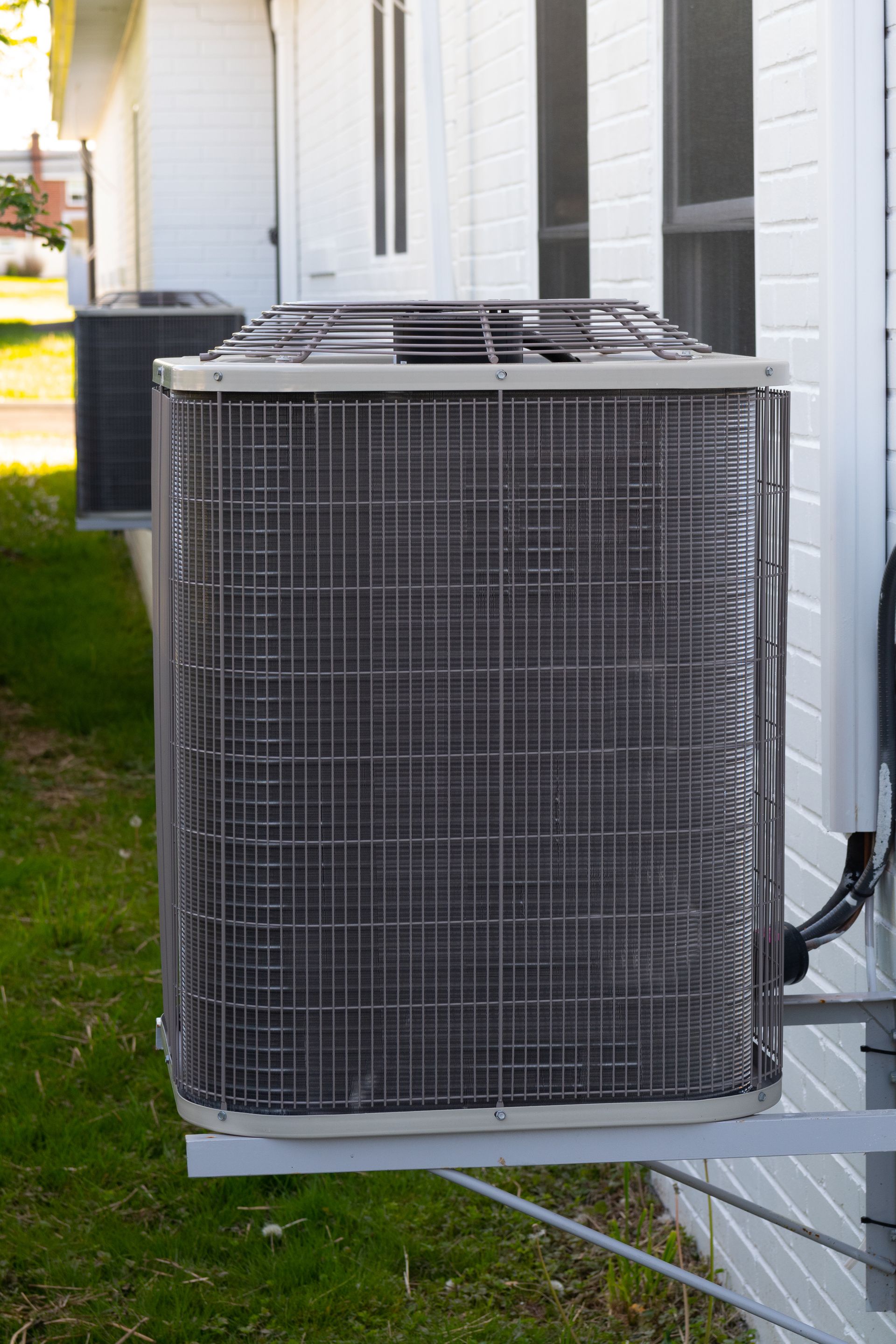 Air conditioning unit mounted on a white building exterior with grass in the foreground.