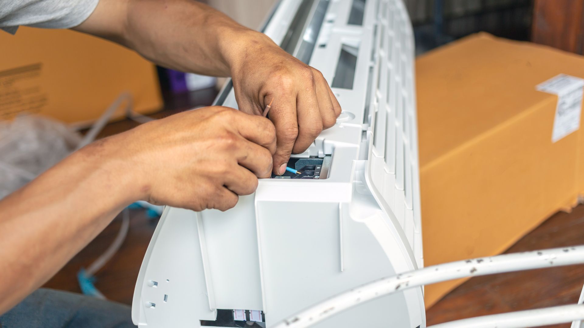 Hands of a repairman working on a white air conditioning unit indoors.