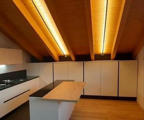 Una cucina moderna con mobili bianchi, un'isola con piano di lavoro nero e ripiano in legno, e soffitti a volta in legno illuminati.