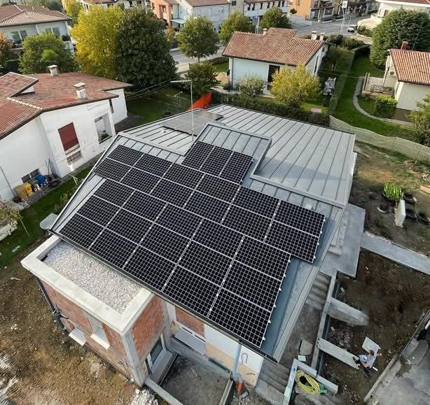 Veduta aerea di un edificio residenziale caratterizzato da una grande serie di pannelli solari neri montati sul tetto metallico grigio.