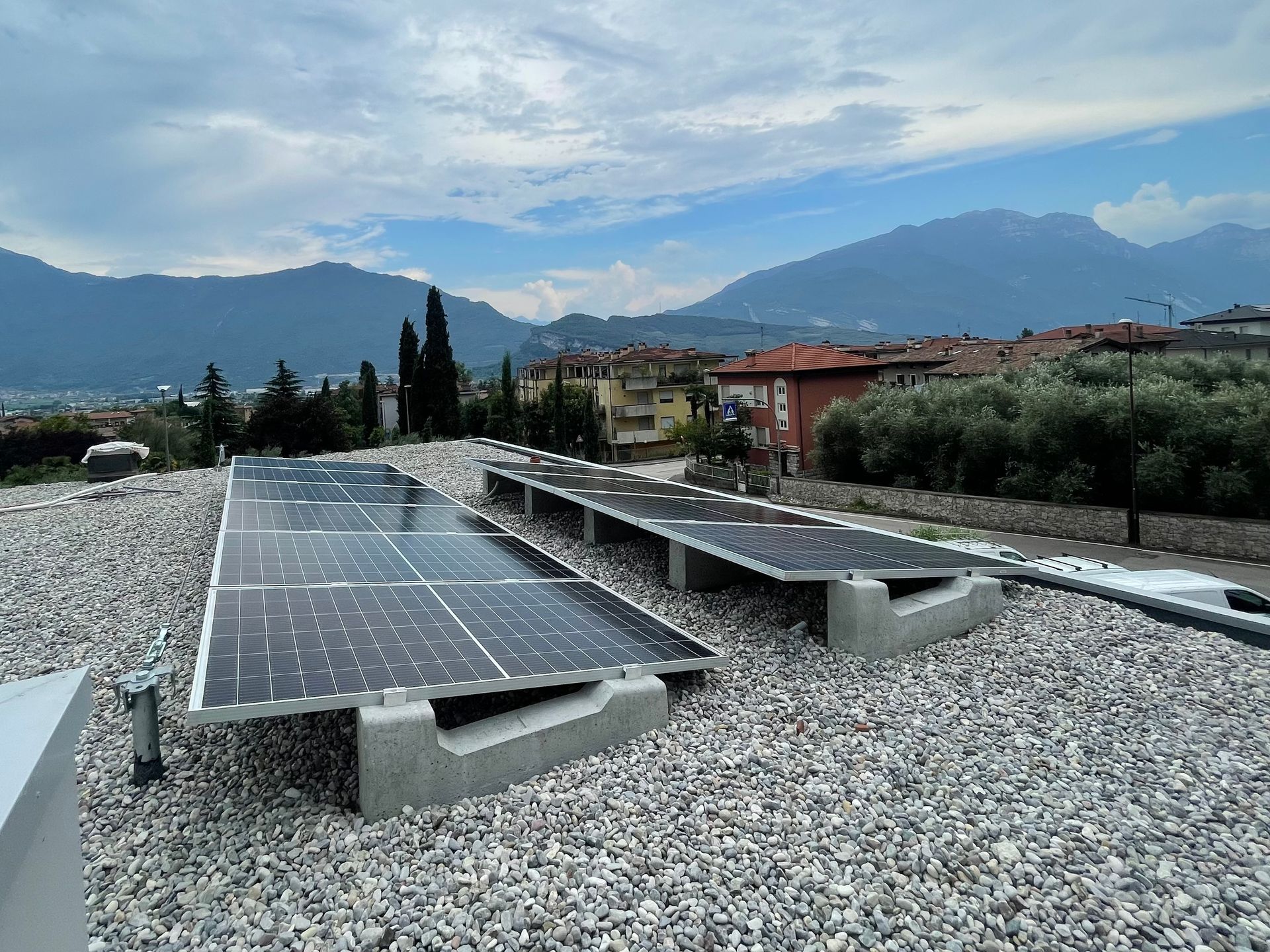 Pannelli solari installati su un tetto piano di ghiaia, con montagne e case sullo sfondo.