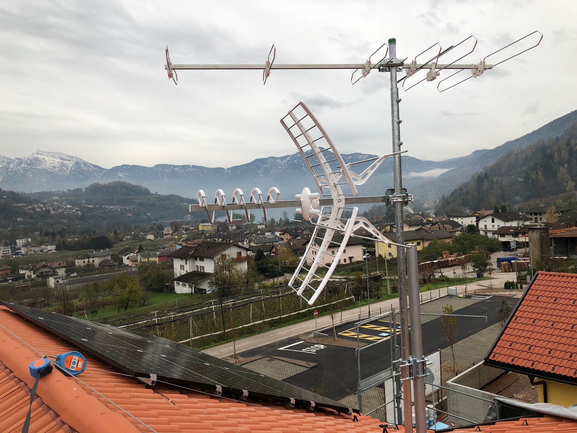 Un'antenna sul tetto installata su un palo metallico, con vista su una cittadina di valle e montagne innevate sullo sfondo.