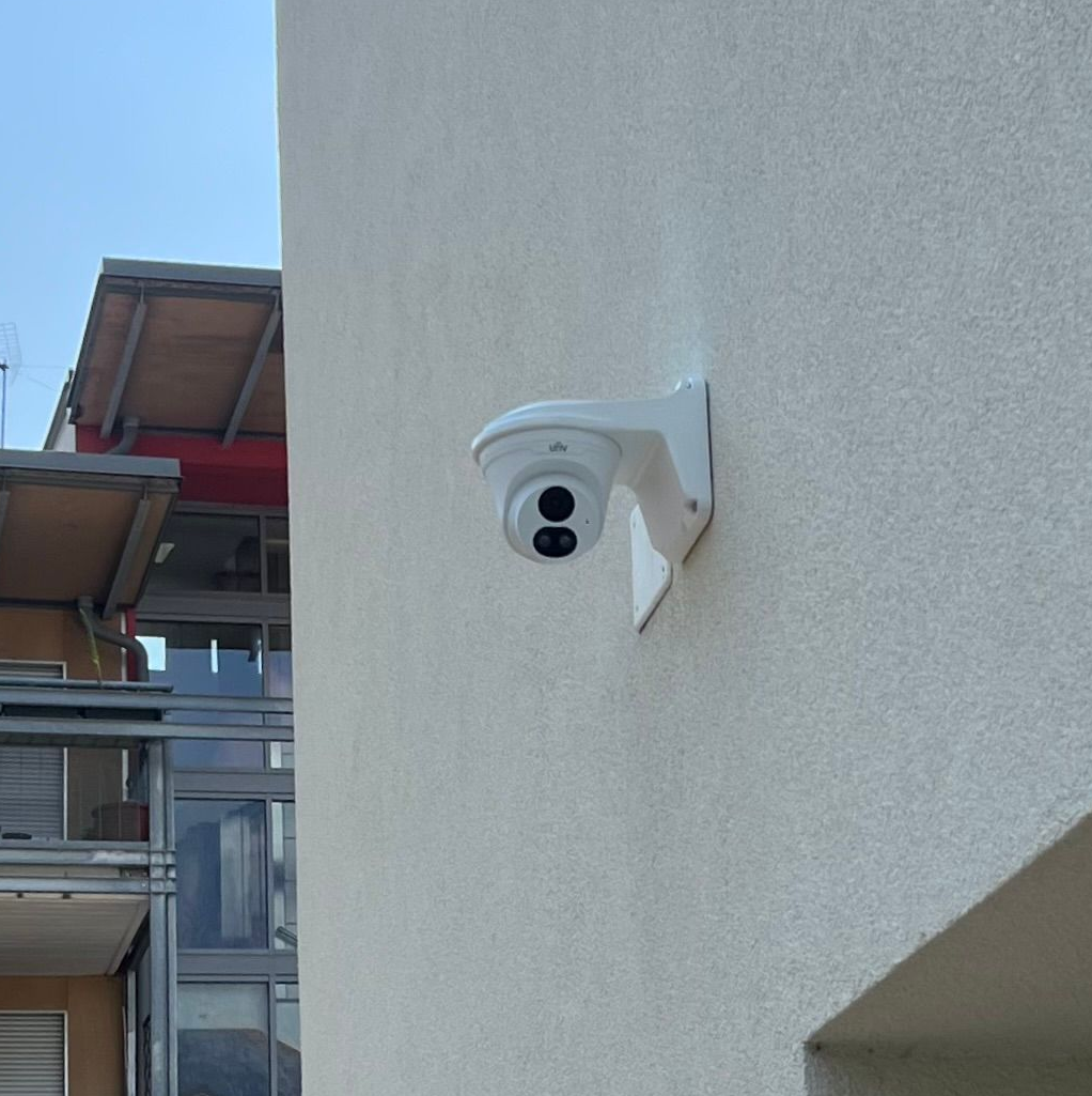 Una telecamera di sorveglianza bianca montata sulla parete esterna intonacata di beige di un edificio.