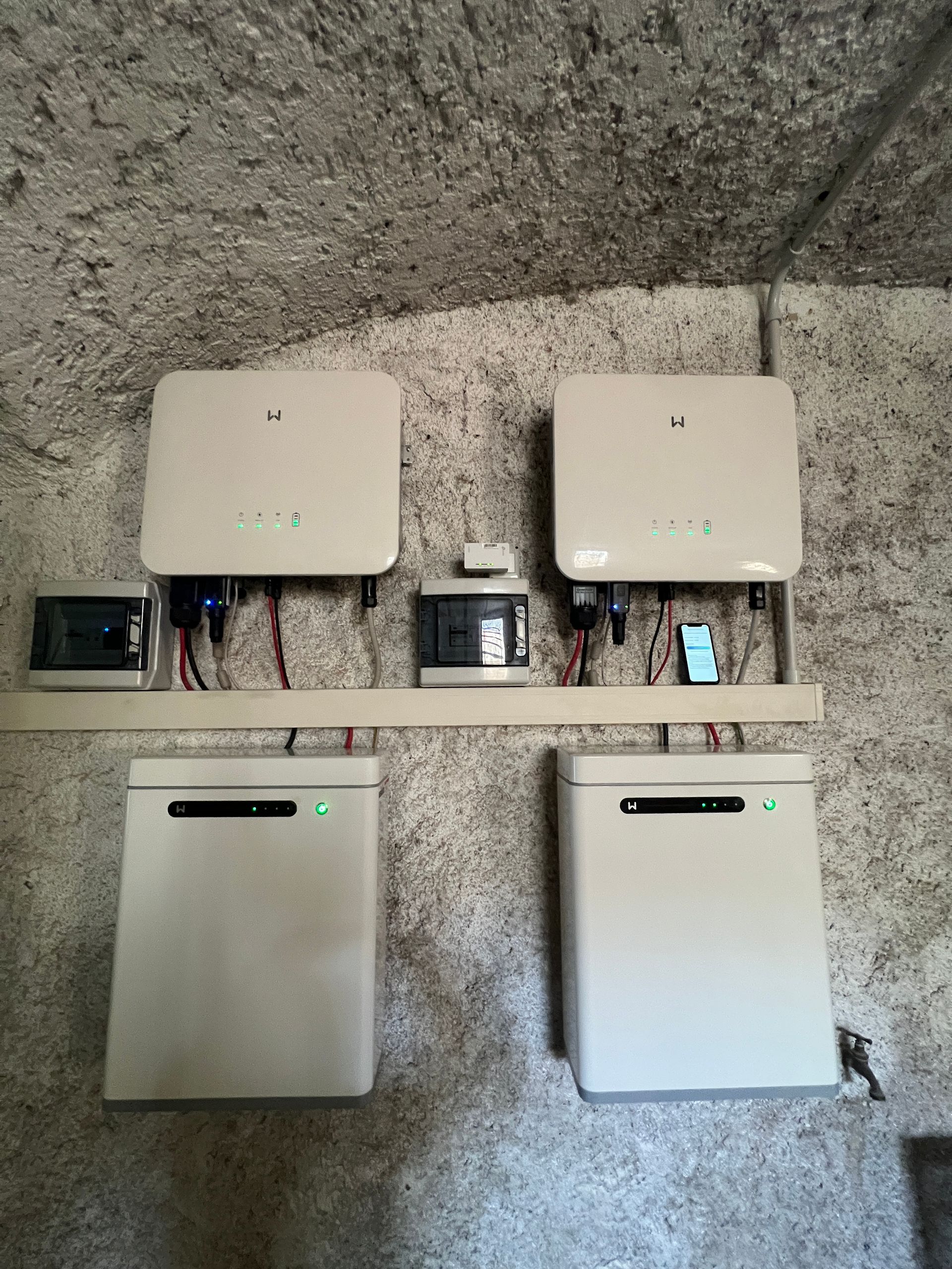 Due inverter solari bianchi e due unità di accumulo a batteria abbinate, montati su un muro di cemento grezzo.