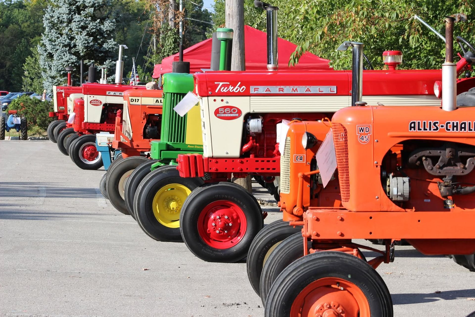 A row of vintage Allis-Chalmers tractors parked on a gravel lot during a sunny day.