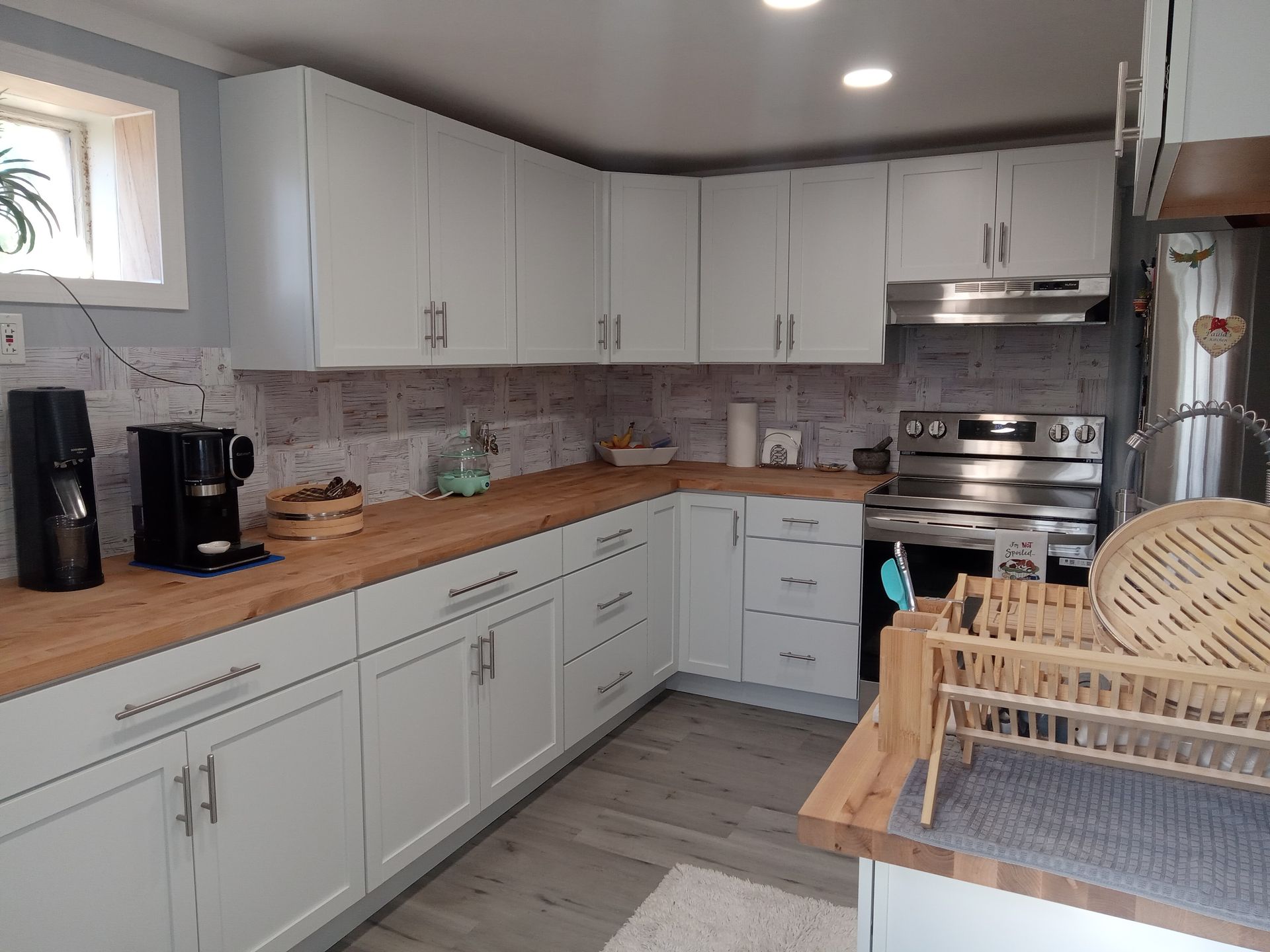 White kitchen cabinets with wood countertops, tile backsplash, and stainless steel appliances.