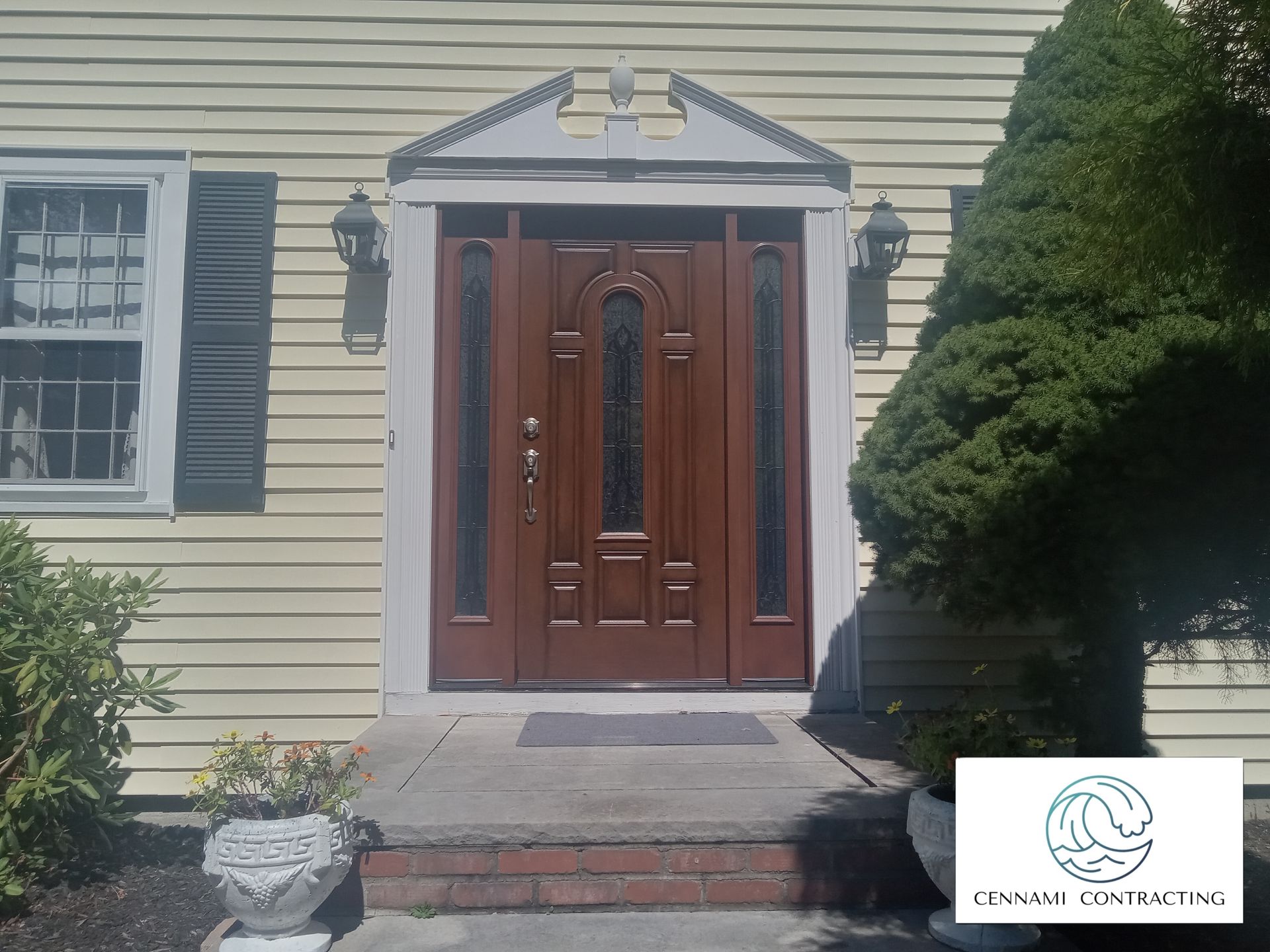 Brown front door with sidelights, under a white trim pediment.