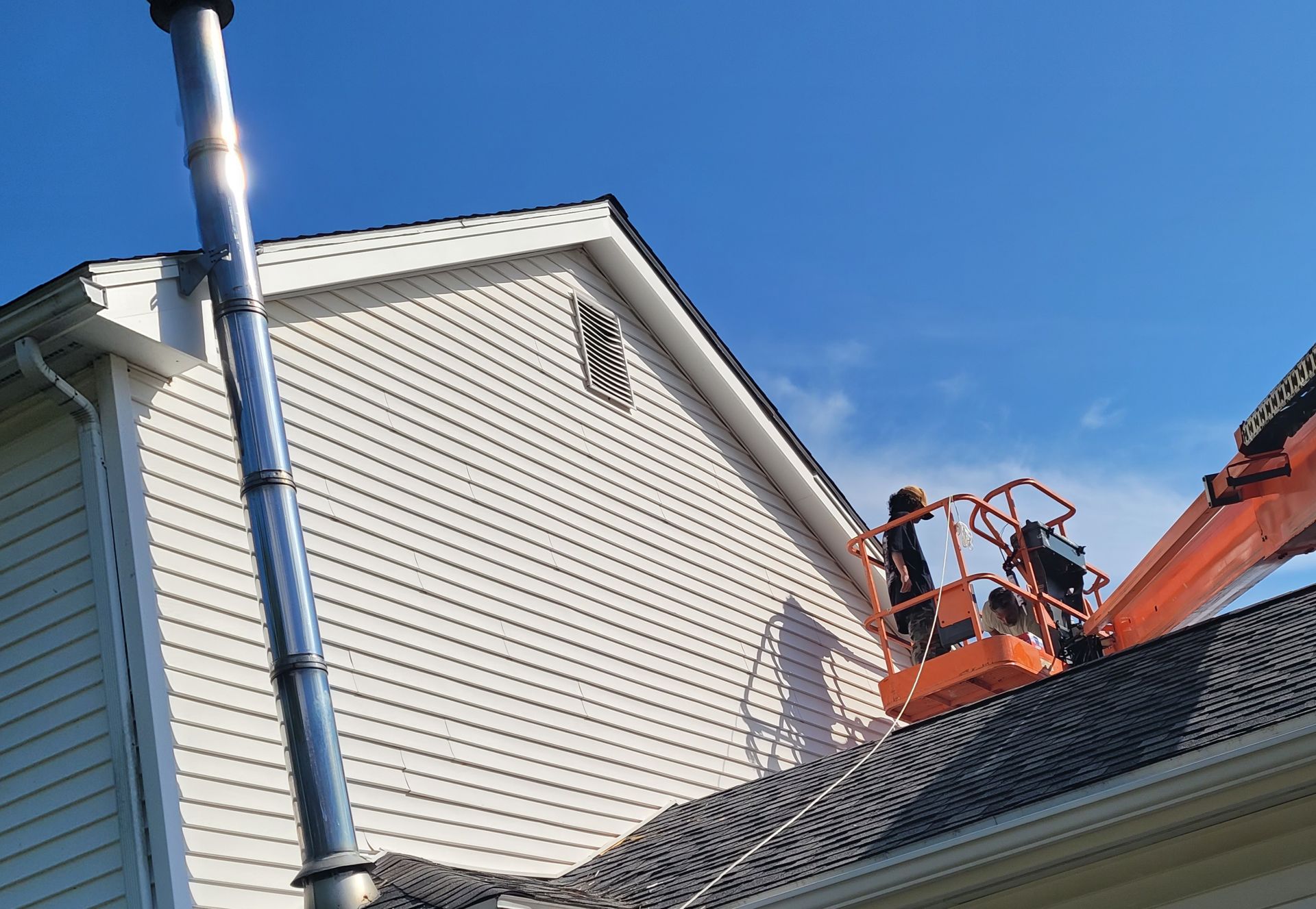 Workers in lift near house with chimney and blue sky.
