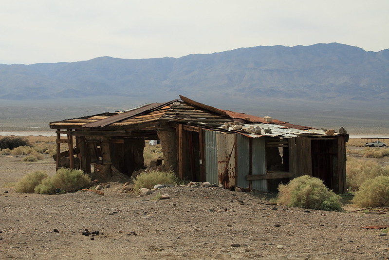An old abandoned house in the desert with mountains in the background