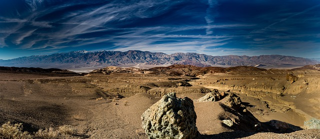 A desert landscape in Death Valley with mountains in the background and a large rock in the foreground.