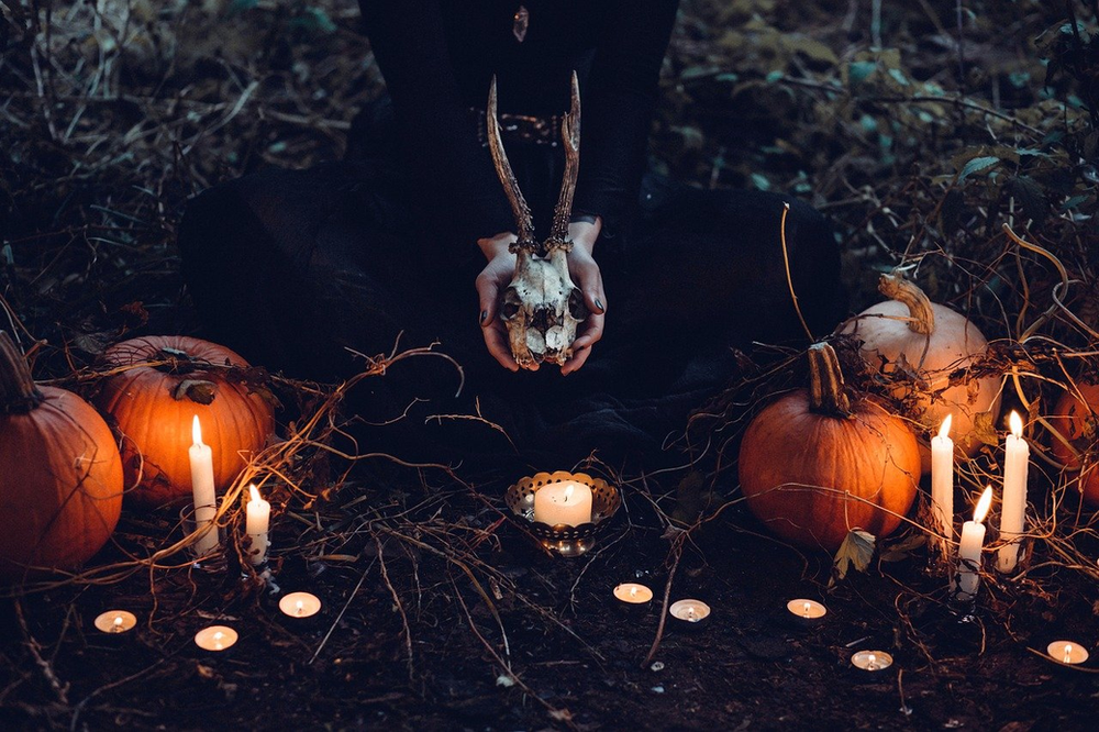 A person is holding a skull in front of pumpkins and candles.