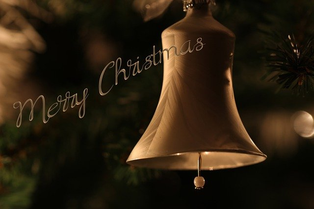 A bell hanging from a christmas tree with merry christmas written on it